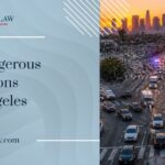 Aerial view of a busy Los Angeles intersection at rush hour, with heavy traffic, multiple lanes converging, and emergency lights in the distance beneath a hazy urban skyline.